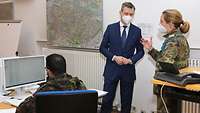 Ein Soldat sitzt am PC, während der Staatssekretär und eine Soldatin über die Arbeit in den Gesundheitsämtern sprechen.