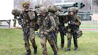 Vier Soldaten mit Waffen, Ausrüstung und Gepäck tragen einen verwundeten Kameraden.