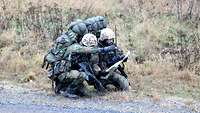 Zwei Soldaten mit Gepäck und Waffen hocken am Wegesrand und orientieren sich mit einer Geländekarte.