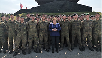 Zwischen vielen Soldaten steht mittig eine Frau in einem blauen Blazer.