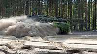 Ein Kampfpanzer wirbelt viel feinen Sand auf, während er über den trockenen Übungsplatz fährt.