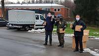 Zwei Militärpfarrer und ein Soldat mit einem Schoko-Nikolaus vor der Kaserne