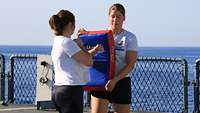 Zwei Frauen in Sportkleidung trainieren auf dem Deck eines Schiffes, im Hintergrund das Meer