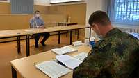 Hinter einer Plexiglasscheibe und mit Mund-Nasen-Schutz sitzt Philipp Paak. Der Prüfer mit großem Abstand unterhält sich mit ihm