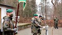 Ein Soldat steht an einem Pult und spricht. Vor ihm und neben ihm stehen Soldaten in Formation.