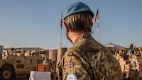 Ein Soldat steht im Vordergrund und blickt zu deutschen und britischen Flaggen, die an einem Fahnenmast im Hintergrund wehen