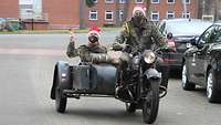 Zwei Soldaten mit Weihnachtsmützen fahren auf einem Motorrad.
