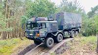 Ein UTF übt auf der Geländefahrbahn. Ein Lastwagen in Flecktarn-Lackierung steht auf einem Hügel.