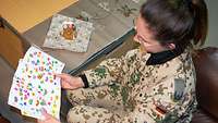 Eine Soldatin sieht sich bunte handbemalte Kinderzeichnungen an