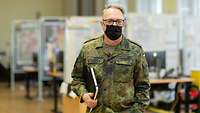 Ein Soldat mit Mund-Nasen-Schutzmaske im Porträt, im Hintrgrund Schreibtische und Whiteboards