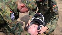 Zwei Soldaten hocken bei einem liegenden Soldaten und nehmen ihm gemeinsam einen Helm ab.
