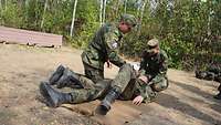 Zwei Soldaten üben an einem am Boden liegenden veretzten dritten Soldaten.
