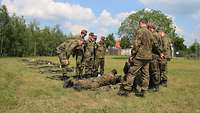 Mehrere Soldaten stehen neben einem Soldaten, der mit einem Gewehr am Boden liegt.