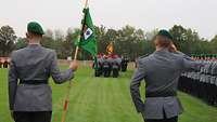 Eine Marschformation mit Musikkorps und die Fahnenabordnung marschieren an den Soldaten vorbei.