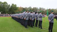 Soldaten sind zum Appell in Linie zu drei Gliedern angetreten, einer hält einen grünen Wimpel.