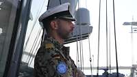 Der Kommandant mit weißer Schirmmütze steht auf einem Schiff 