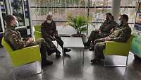 Vier Soldaten sitzen in einem Foyer in Sesseln und unterhalten sich