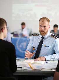 Ein Soldat sitzt mit Jugendlichen an einem Tisch und spricht zu ihnen