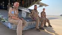 Zwei Soldaten und eine Soldatin sitzen auf der Laderampe eines Flugzeuges