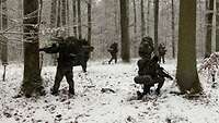 Sechs Soldaten haben sich in einem verschneiten Waldstück verteilt.