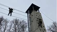 Ein Soldat überwindet einen grauen Kletterturm, ein zweiter einen anschließenden, doppelten Seilsteg. 