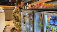 Ein Soldat kniet vor einem Kühlschrank und befüllt diesen mit Getränkedosen