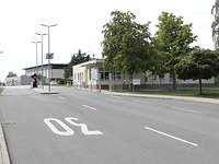 Eine asphaltierte Straße läuft auf ein Wachhaus zu. Die Straße ist mit zwei Schlagbäumen gesperrt.
