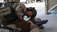 Ein Soldat kniet über einem am Boden liegenden Soldaten und überprüft seine Atmung