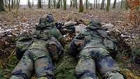 Zwei Soldaten liegen in einer selbstgebauten Stellung im Wald.