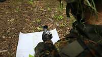 Blick über die Schulter eines Soldaten, der eine Karte und einen Kompass in dern Händen hält.