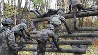 Mehrere Soldaten erklimmen hinter- und nebeneinander ein Sprunggerüst aus Holz.