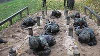 Sieben Soldaten kriechen auf Sand unter flach gespannten Drähten durch.