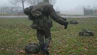 Ein Soldat schleppt einen verwundeten Kameraden auf seinen Schultern über eine Wiese im Nebel.