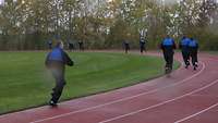 Mehrere Soldaten laufen bei Regen in blauen Sportanzügen auf einer roten Tartanbahn.