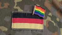 Ein Anstecker mit dem Motiv einer Regenbogenflagge über einer Deutschlandflagge auf einer Bundeswehr-Flecktarn-Uniform