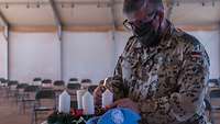 Ein Soldat steht vor einem Adventskranz und entzündet die zweite Kerze in einem großen Zelt 