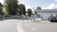 Haupttor der Kaserne Eine Straße läuft auf den Kaserneneingang mit zwei Schranken zu, rechts ein weißes Wachgebäude.