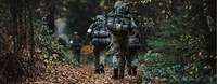 Soldaten, von hinten gesehen, laufen mit ihrer Ausrüstung einen Waldweg entlang