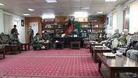 In einem Raum mit rotem Teppich, Holztischen, Sofas und Sesseln sitzen mehrere deutsche und afghanische Soldaten 