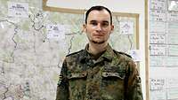 Ein Soldat in Flecktarnuniform steht vor einer großen Lagekarte, auf der mehrere Hinweisschilder angebracht sind. 