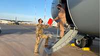 Ein Soldat übergibt an einer Flugzeugtreppe eine rote Mappe an einen weiteren Soldaten, der auf der Treppe steht