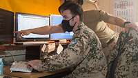 Ein Soldat sitzt vor einem Rechner, ein zweiter Soldat zeigt ihm etwas auf dem Bildschirm
