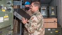 Zwei Soldaten stehen in einem Container und heben ein technisches Gerät in ein Regal