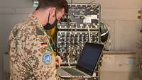 Ein Soldat steht vor dem Netzwerkschrank und hält einen Laptop in der Hand