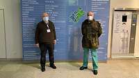Ein Soldat und ein weiterer Mann stehen mit Muschutz und Abstand vor dem Liegenschaftplan des Krankenhauses