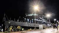 Ein kleines graues Kriegsschiff liegt an einer Pier bei Nacht.