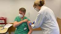 A doctor inserts a needle into a man’s upper arm.