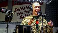 Ein Soldat mit Kopfhörern steht in einem Tonstudio vor einem Mikrofon