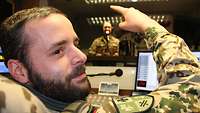 Ein Soldat sitzt am Regiepult und zeigt mit dem Finger auf einen Soldaten, der am Mikrofon vor ihm steht