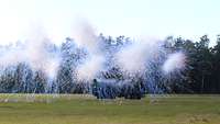 Smoke pots exploding in front of a palletized load system truck A vehicle on a field, a smoke screen building up in front of it.